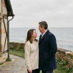 Couple sur la terrasse d'une maison normande en pierre avec vue sur la Manche, illustrant l'achat d'une maison en bord de mer en Normandie
